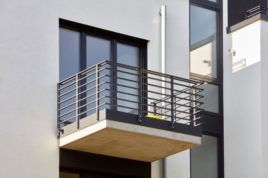 Balkon mit schwarzer Metallbrüstung und Fenstern mit weißer Fassade