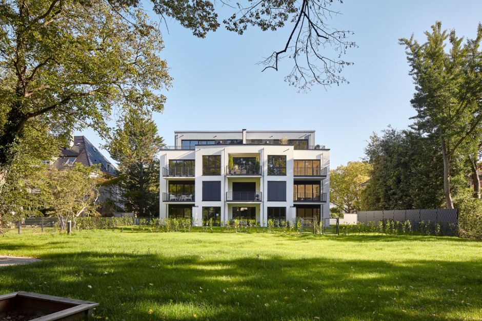 Frontalansicht der Rückseite eines neuen Mehrfamilienhaus mit moderner Architektur und riesigem Garten vor hellblauem Himmel in Köln Braunsfeld