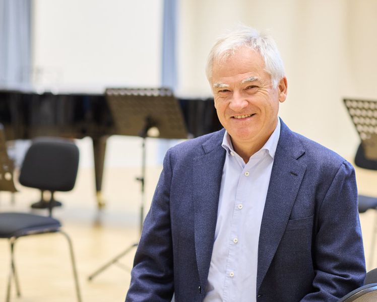 Altexander Pirlet sitzend in einem Klassenraum der Rheinischen Musikschule Köln vor mit Stühlen und Notenständern